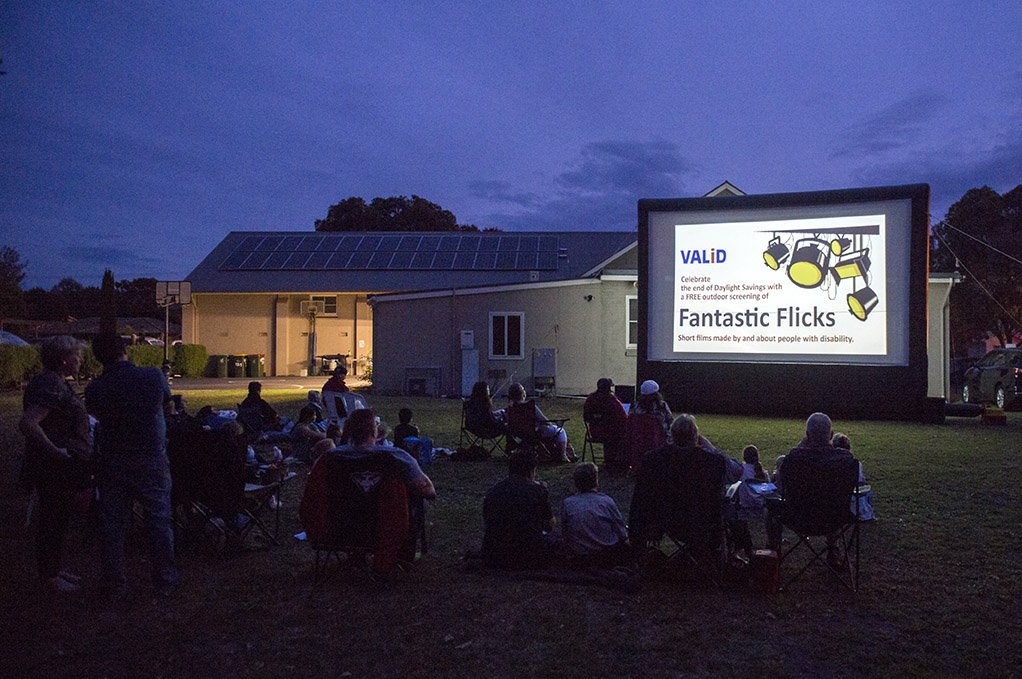 people sitting outside at dusk looking at a projector promoting FANTASTIC FLICKS