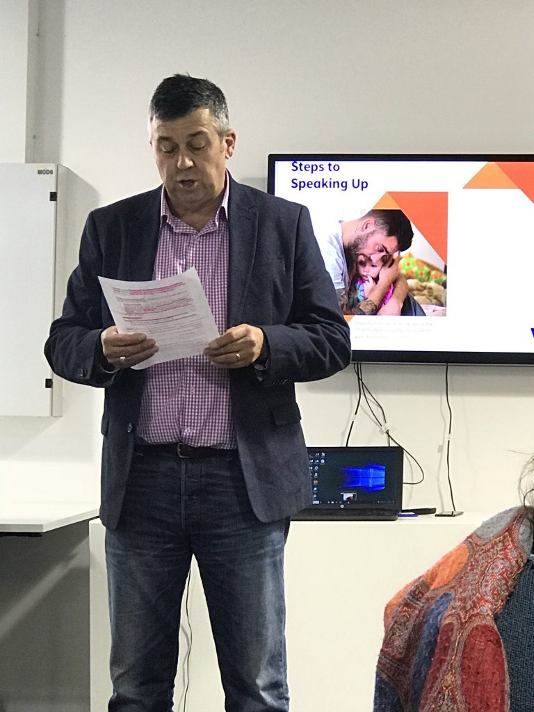 David standing in front of group of people reading from an A4 piece of paper